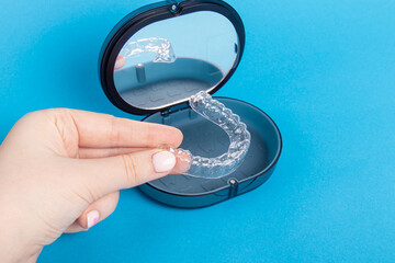 Woman holds aligners on blue background. Dental container-case for storing aligners