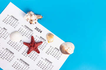 Red starfish, seashells and calendar on blue background. Top view. Vacation planning