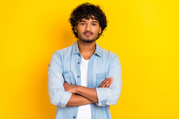 Photo of good mood serious handsome man with curly hairdo dressed denim shirt holding palms crossed isolated on yellow color background