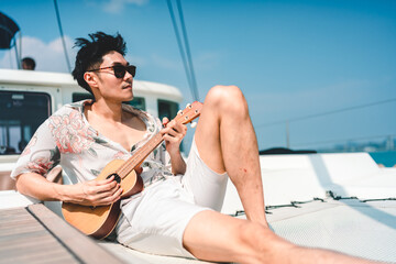 Outdoor travel lifestyle concept, Asian man playing ukulele or guitar music in holiday vacation,...