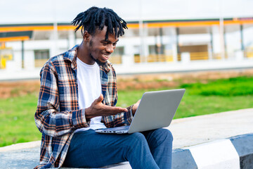 Photo of a cheerful young black African man on dreadlocks working on laptop