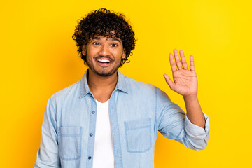 Photo of satisfied cheerful young man toothy smile arm palm waving hi isolated on yellow color background © deagreez