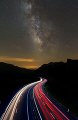 Cars driving fast on the highway with the stars in the night sky.