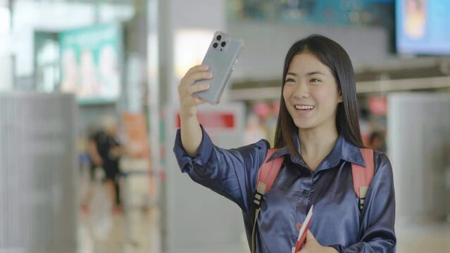 Girl with a backpack talking on video coll through mobile phone at the airport. posing for selfie on smartphone camera, Asian woman enjoying radio broadcast making photo for picture