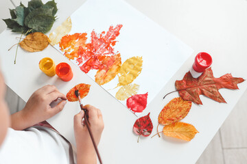 Little girl painting on autumn yellow leaves with gouache, kids arts, children creativity, autumn...