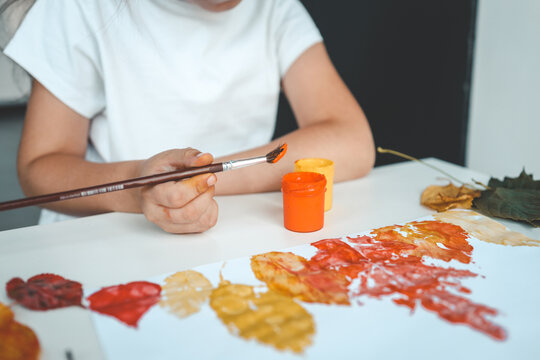 Little girl painting on autumn yellow leaves with gouache, kids arts, children creativity, autumn art