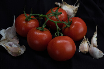 bunch of tomatoes and garlic on a black background.