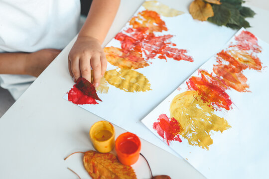 Little girl painting on autumn yellow leaves with gouache, kids arts, children creativity, autumn art