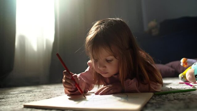 Capturing the Magic of Childhood: Little Girl Engaged in Pencil Drawing on Paper while Sitting Comfortably on the Living Room Floor. High quality 4k footage