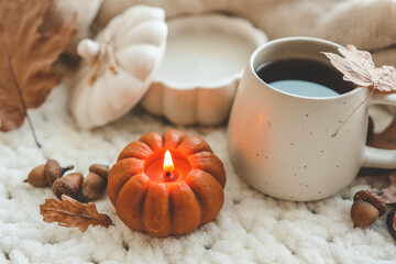 Burning candle in the shape of a pumpkin and a cup of tea, autumn mood