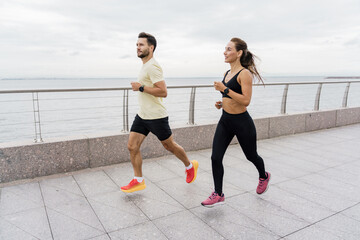 Athletes are strong people who work out jogging together. Runners are a man and a woman in sportswear and running shoes, in full height. Using a fitness watch.