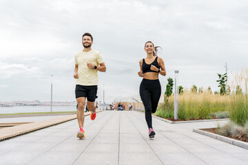 A personal trainer and a client teach fitness running.  Male and female runners smile and train together. Instructors of friends use a fitness watch and a sports app.  