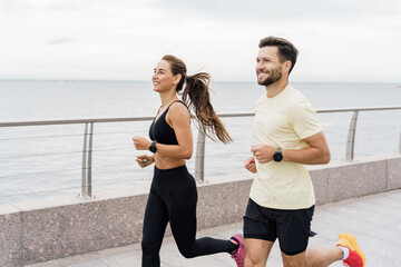 Male and female runners smile and train together. A personal trainer and a client teach fitness running. Instructors of friends use a fitness watch and a sports app. 