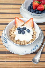 A fresh healthy breakfast with berries, oats and yogurt in an elegant porcelain bowl on a bamboo mat. Healthy eating.
