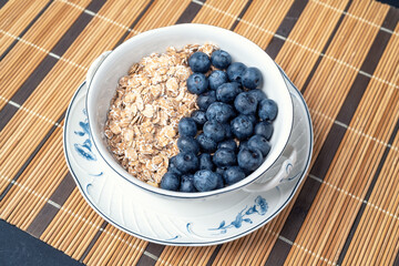 A fresh healthy breakfast with berries and oats in an elegant porcelain bowl on a bamboo mat. Healthy eating.