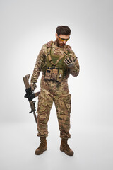 Wounded military infantry in body armor checking chest, if there any injury. Front view of discouraged male soldier in uniform covering laceration with hand, isolated on gray. Injury, war concept.