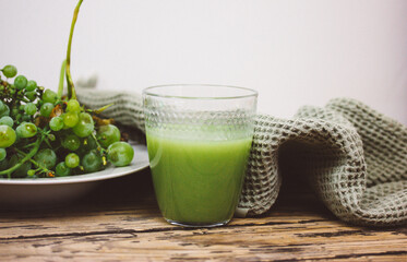 A branch of green grapes and a glass of freshly squeezed grape juice on a wooden table. Rustic still life with natural healthy refreshment drink, beverage. Healthy useful detox smoothie.