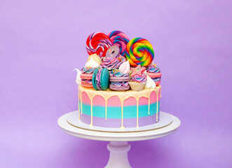 Cololrful and bright birthday cake with lollipops and sweets over a purple background with copy space