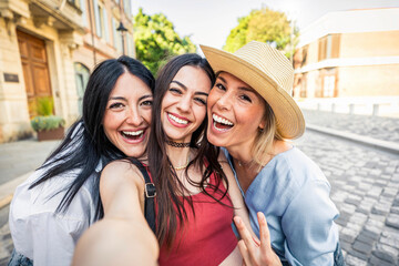 Happy female friends taking selfie with smart mobile phone device outside - Delightful young women having fun on summer vacation - Friendship concept with ladies enjoying day out - obrazy, fototapety, plakaty
