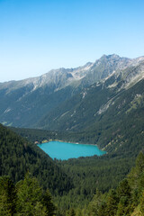 Aerial view of turquoise alpine mountain lake Lago di Anterselva (Antholzer See) as seen from Passo Stalle (Staller Pass) in a Dolomite mountain valley with green pine forest - obrazy, fototapety, plakaty