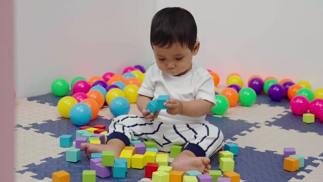 infant baby playing wooden block toy in playpen at home
