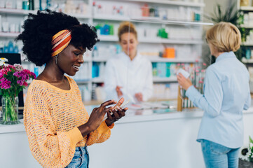 African american woman using a smartphone while shopping in a pharmacy