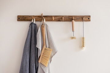 Wood hook rack with tea towels, broom and dish bottle brush hanging on a white wall on the modern...