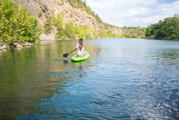 Fototapeta na wymiar a teenage girl rides on a green SUP board on a beautiful mountain lake, Krasnosulinsky canyon in the Rostov region, in Russia.