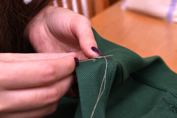 woman sewing with needle and thread a button on a green t-shirt
