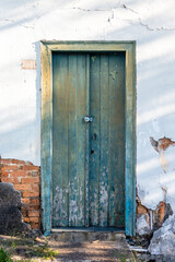 Aged and damaged door in a rustic style on the wall of the abandoned rural house. Blue wooden door. Diamantina, Minas Gerais, Brazil