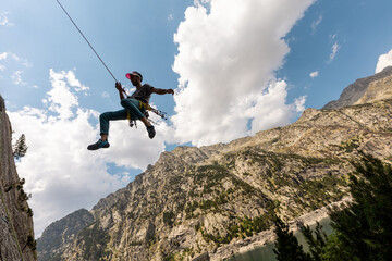 Person climbing in high mountains with yellow jacket rope and helmet in nature, confidence and risk, safety