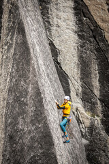 Person climbing in high mountains with yellow jacket rope and helmet in nature, confidence and risk, safety