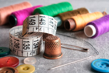 Sewing kit of needle, thimble, thread and measuring meter.On gray concrete table top.