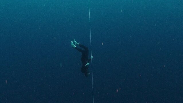 Male freediver descends along the rope during freedive training session in open sea and free falling in to the darkness