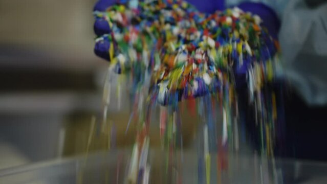Close-up female hands raising shredded multicolored plastic garbage with parts falling down in box. Closeup unrecognizable young woman in uniform sorting processed trash on recycling station