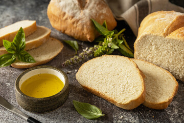 Sliced Italian ciabatta bread with extra virgin olive oil and herb on a dark stone background....