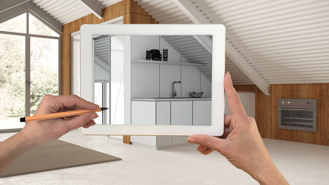 Hands holding and drawing on tablet showing minimal mezzanine mansard kitchen details CAD sketch. Real finished interior in the background, architecture design presentation