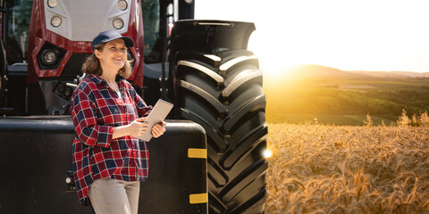 Woman farmer with a digital tablet on the background of an agricultural tractor