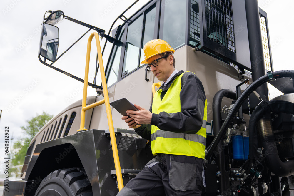 Poster engineer with tablet computer stands on the stairs to the cab of a truck.