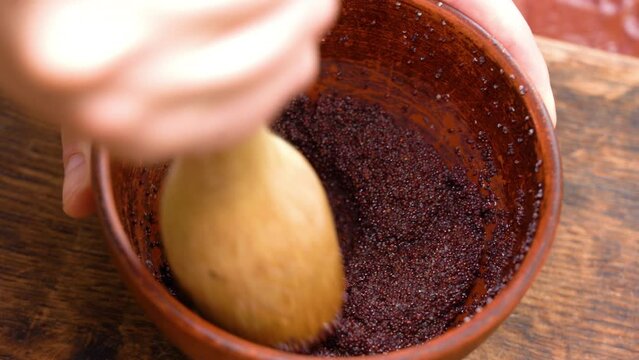 poppy seeds with water, in a brown mask, are kneaded with a wooden masher