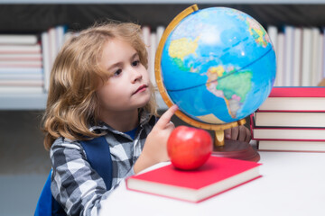 Explorer and discovery. School pupil looking at globe in library at the elementary school. World globe. Kid boy from elementary school with book. Concept of education and learning.