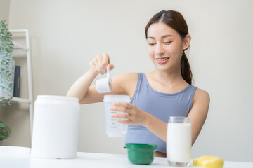 Fototapeta na wymiar Diet meal replacement for weight loss, smile asian young woman, girl in sportswear, hand in holding scoop making protein shake, drink supplement for muscle after workout at home. Healthy body care.