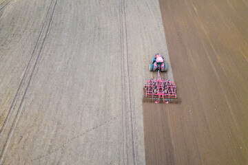 A tractor with a trailer plough plows a farmer's field from a aerial view. Top view of working rural machinery and a plowed field. Unmanned management and control system for work in the agricultural