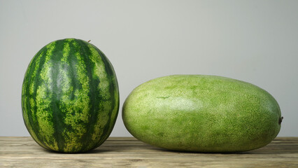 Two watermelons of different varieties lie on a wooden table.