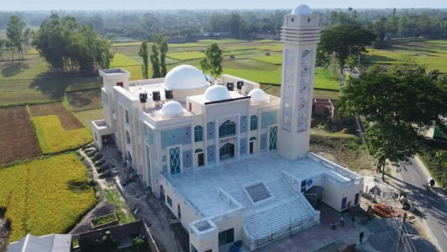Drone footage circling Bangladesh's stunning holy model mosque in the midst of woods and rice fields, beside road