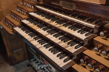 Fototapeta na wymiar Large keyboard of a church organ. Manuals, pedalboard and many registers. Classical music, conservatory and sacred music. Old wooden organ connected to pipes.