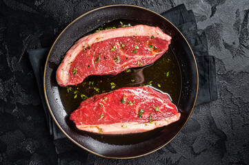 Raw marbled beef meat  steak marinated with olive oil, thyme, salt and pepper. Black background. Top view