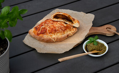 Cutted pizza calzone with tomato sauce, green pesto and cheese on wooden plate