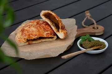 Cutted pizza calzone with tomato sauce, green pesto and cheese on wooden plate