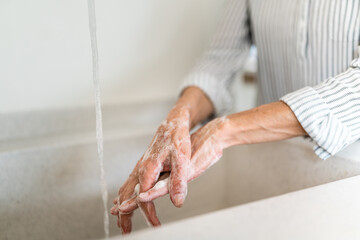 Closeup photo of senior older woman thoroughly scrubbing her hands with soap.